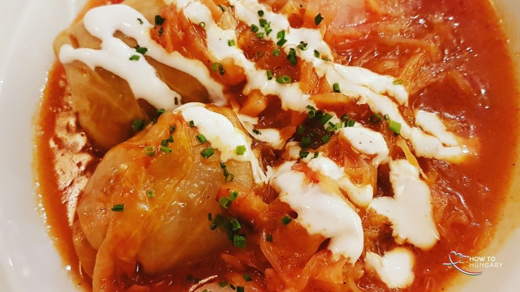 Close-up photo of steaming Hungarian stuffed cabbage rolls (töltött káposzta) on a festive Christmas plate, wrapped in fermented cabbage leaves filled with minced pork and rice, nestled in sauerkraut and tomato sauce, topped with sour cream, evoking holiday warmth and tradition