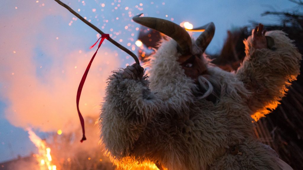 Busós in traditional wooden masks and sheepskins standing near a bonfire during Busójárás in Mohács