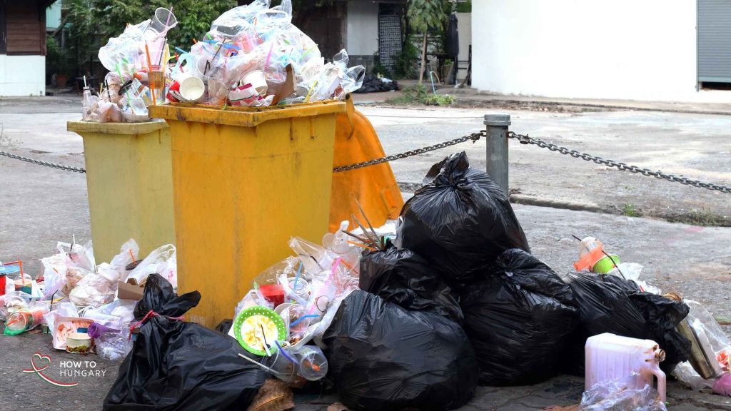 Overflowing rubbish bins and scattered garbage on a Budapest street, showing the impact of collection delays and bottle hunters during Hungary’s bottle deposit return system rollout.
